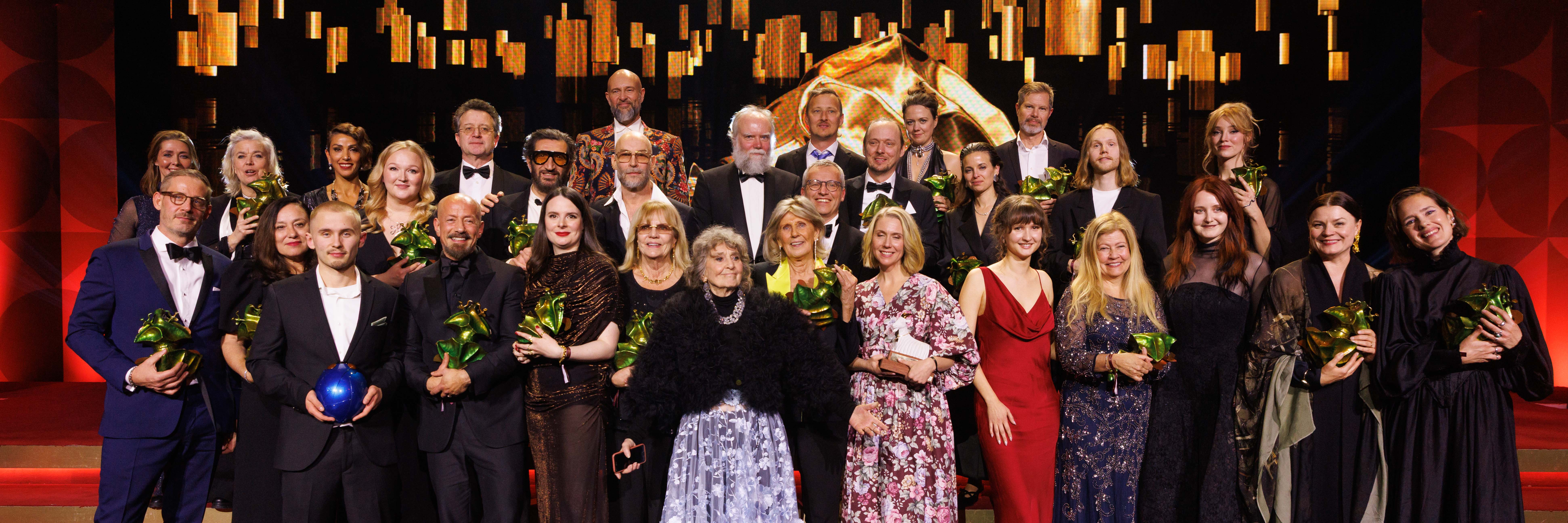 En grupp glada, finklädda människor står på en scen.