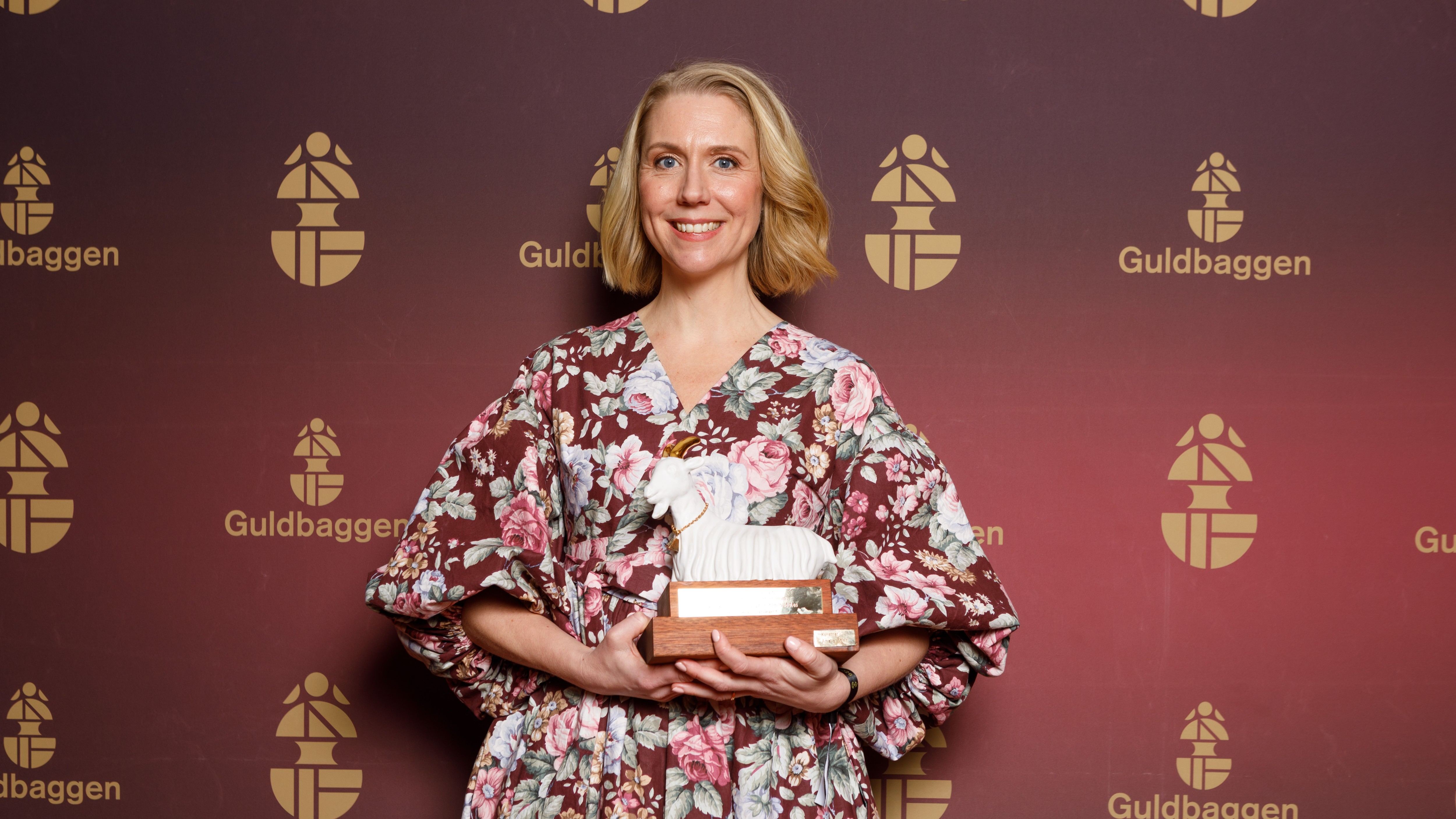 En glad kvinna står med en statyett i form av en get.