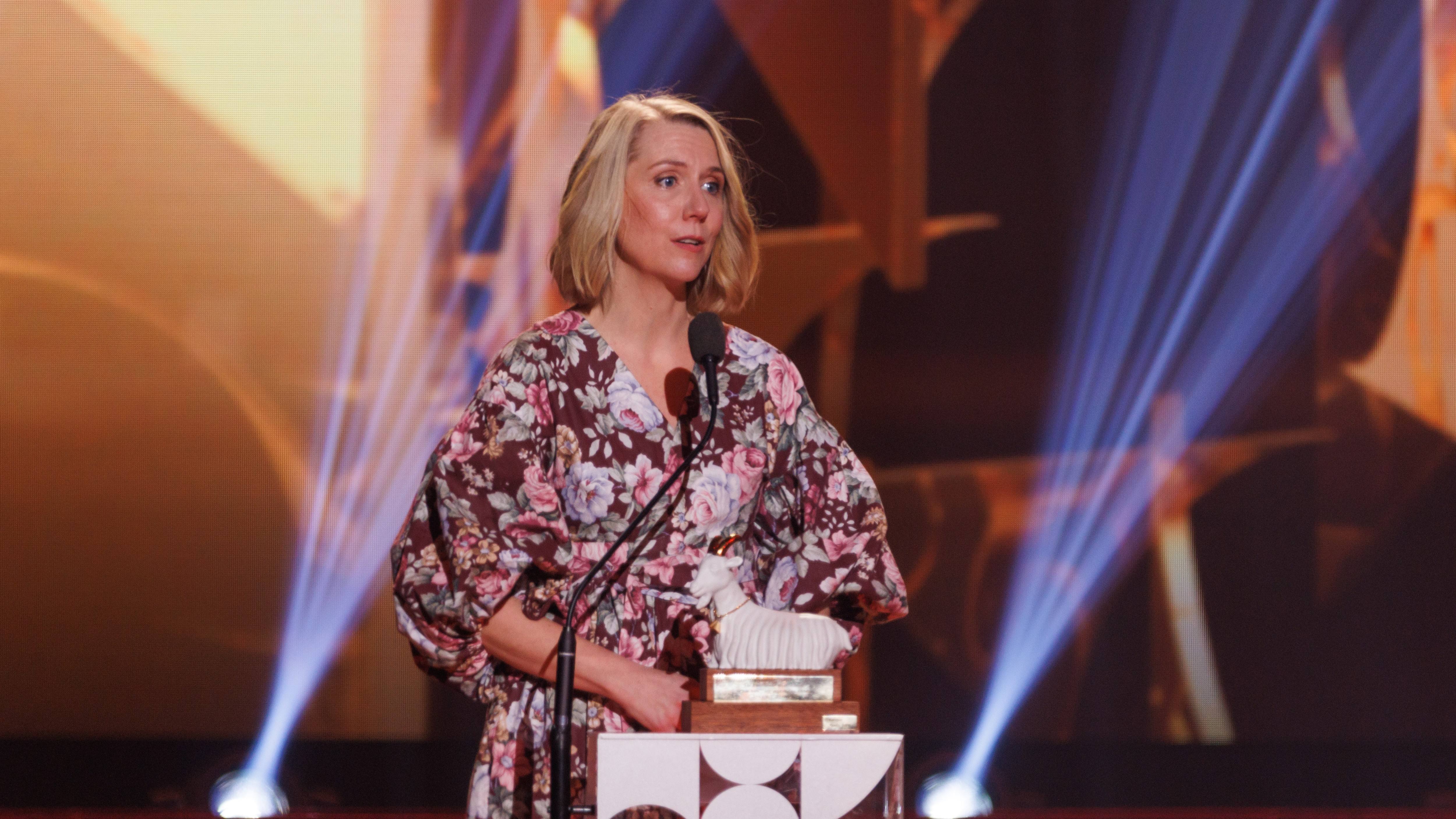 En kvinna talar på scen och håller en Get-statyett.