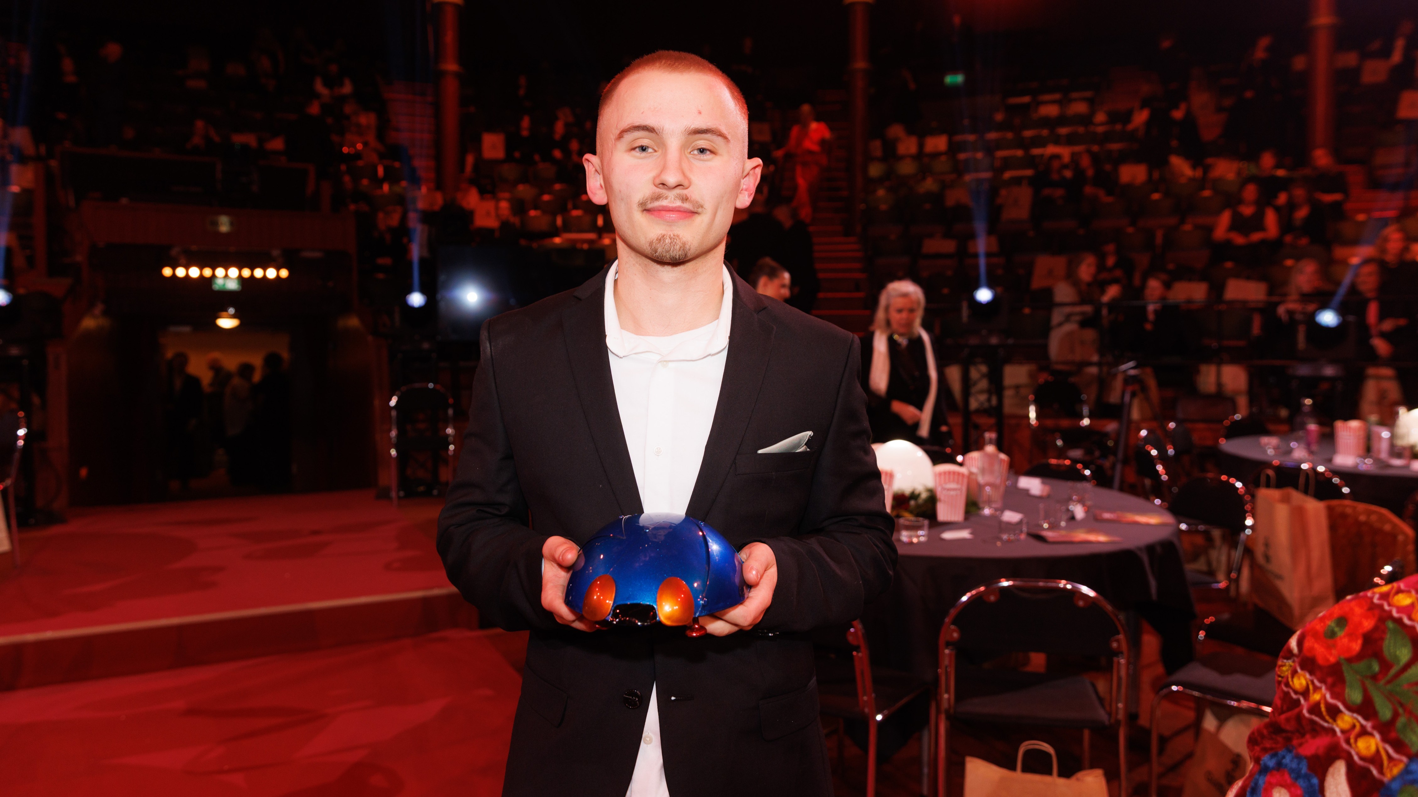 En ung man håller upp en blå statyett i form av en guldpiga.