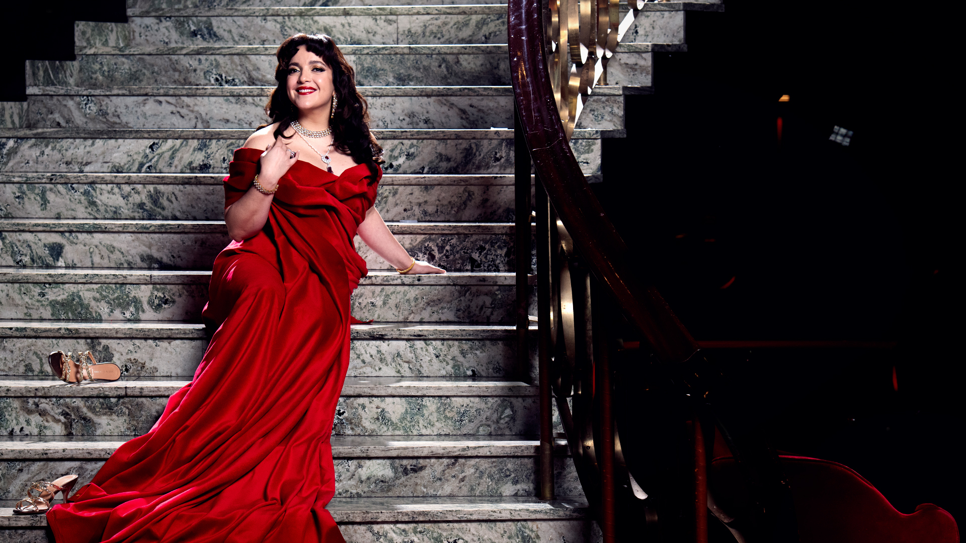En kvinna lång, röd klänning sitter i en marmortrappa.
